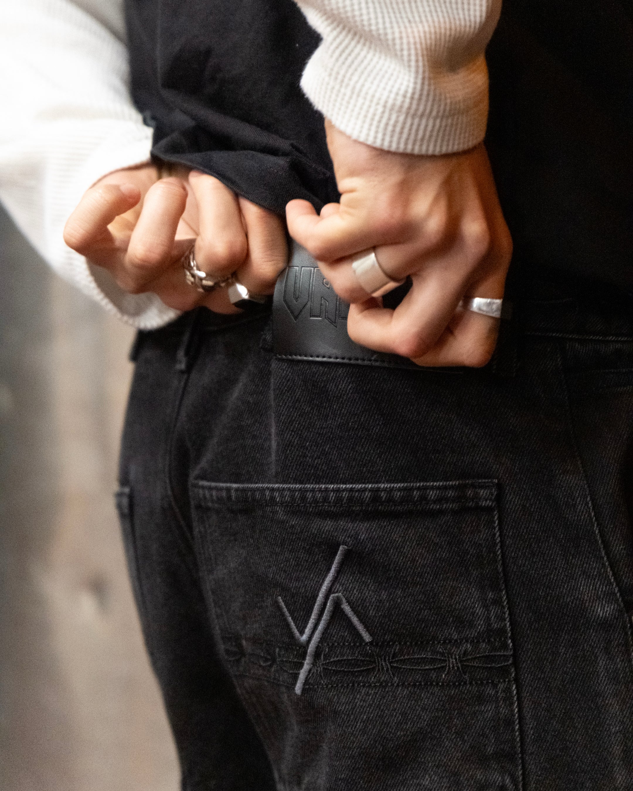 Close up shot of the Model wearing the deadweight denim jeans by valour apparel, showcasing the dark grey logo and black barb wire embroidery in the back pocket.